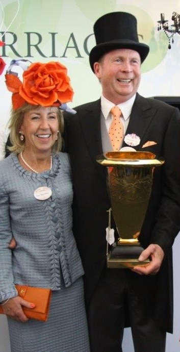 A smiling, well dressed woman and man holding a trophy